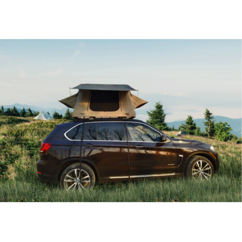 A tan deluxe rooftop tent mounted on a SUV in a scenic mountain landscape during sunset.