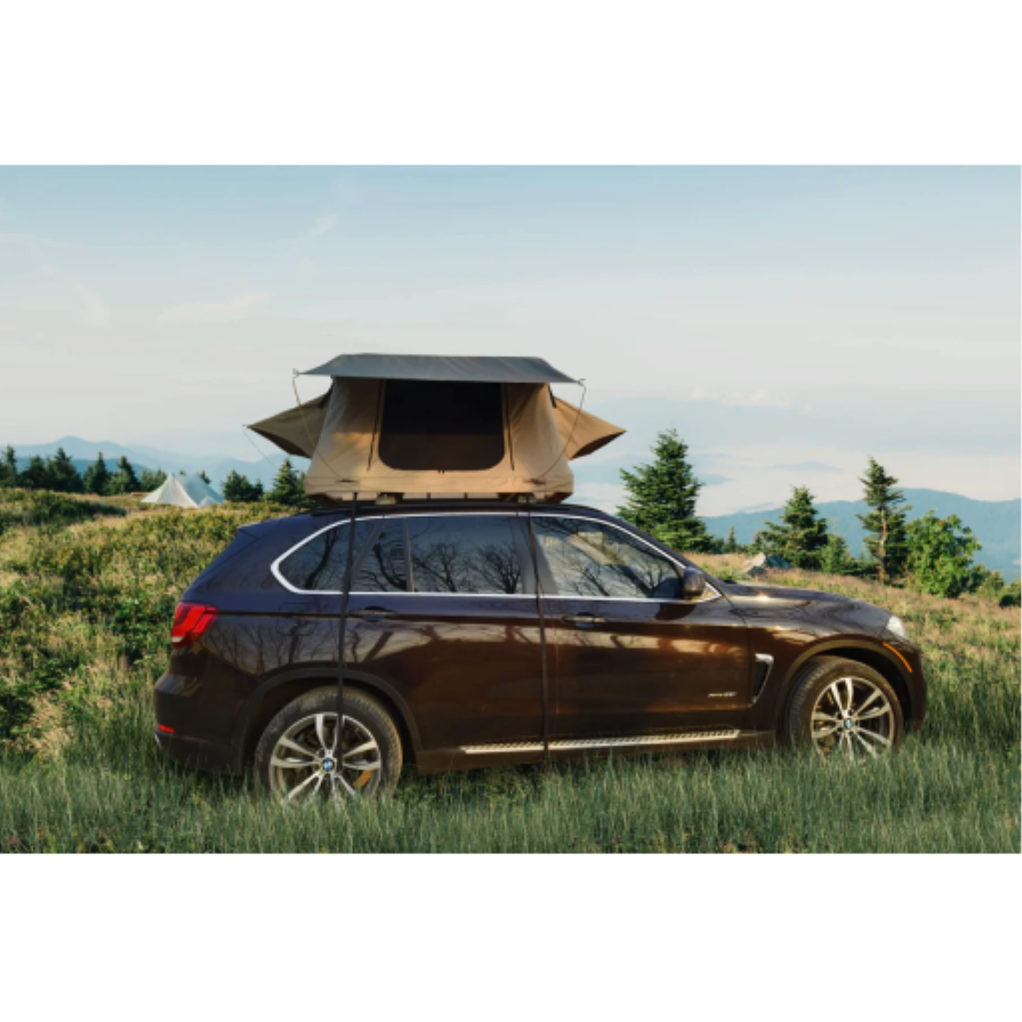A tan deluxe rooftop tent mounted on a brown SUV parked in a scenic mountain meadow.