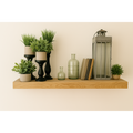 Honey floating wood shelf decorated with green plants, glass bottles, and a lantern.